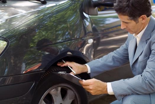 A man with a checklist looking at a tyre of a car